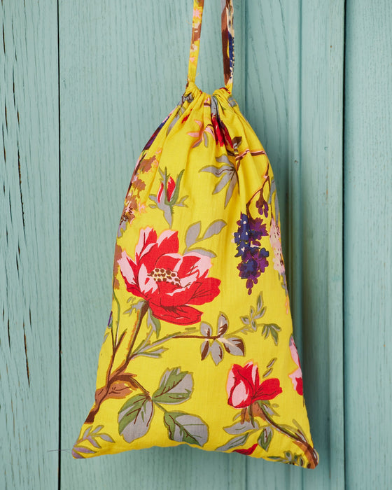 Yellow drawstring bag with floral pattern hanging on a light blue wooden panel.