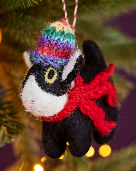 Felt black and white cat ornament with a colorful hat and red scarf hanging on a Christmas tree.