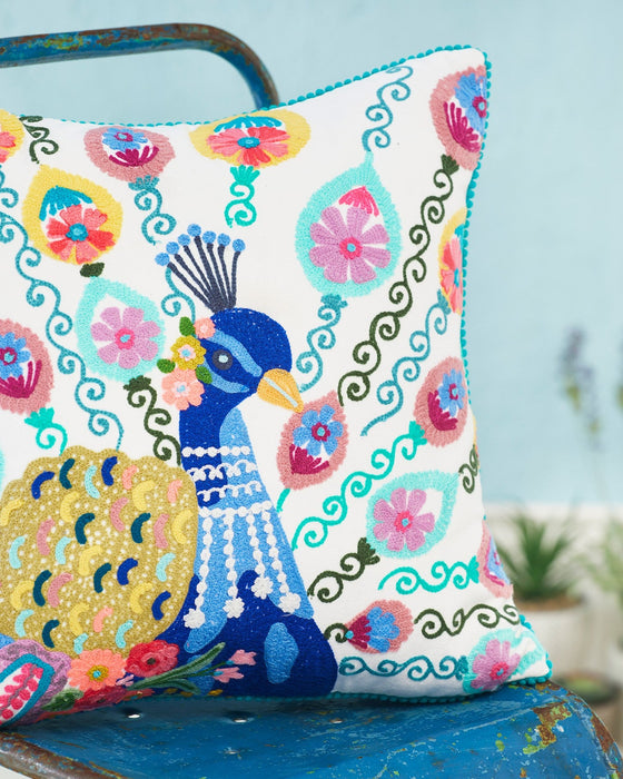 Decorative pillow with peacock design on a blue chair against a light blue background