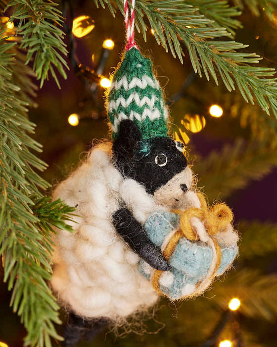 Knitted sheep decoration with a green hat hanging on a Christmas tree.
