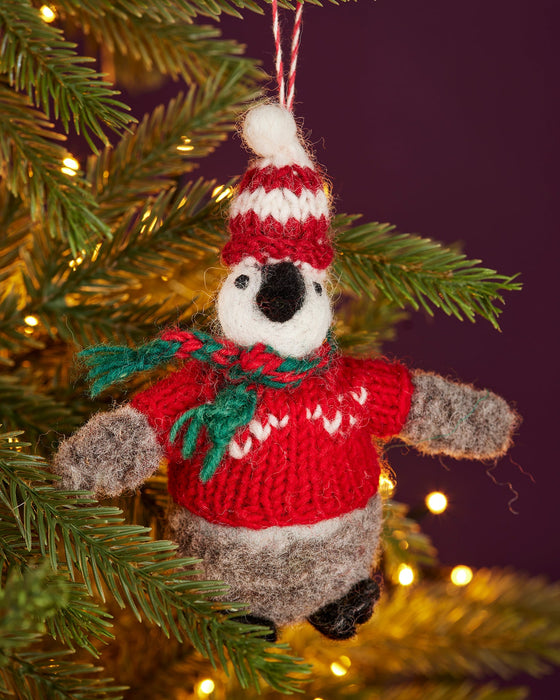 Felt baby penguin Christmas decoration wearing a red sweater and hat, hanging on a Christmas tree.