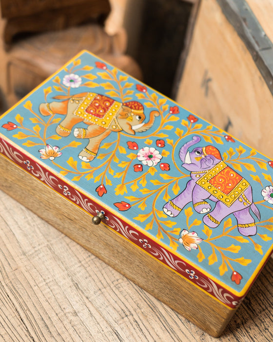Decorative wooden box with painted elephants and floral patterns on a wooden surface.