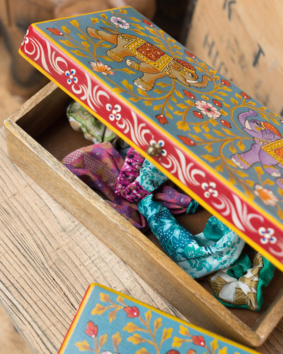 Decorative box with colorful fabric items inside, featuring an elephant design on the lid.