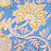A detailed close up picture of the Aasmani hand-block-printed cotton tablecloth with pink and yellow botanicals on a dusty blue background