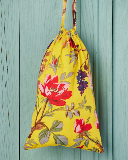 Yellow drawstring bag with floral pattern hanging on a light blue wooden panel.