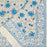 Floral-patterned fabric with blue and white flowers on a beige background, folded at one corner to show the border design