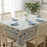 A dining table featuring a stylised floral block-print tablecloth in a blue, teal and warm sand. The table is set with white plates and slate-blue napkins.