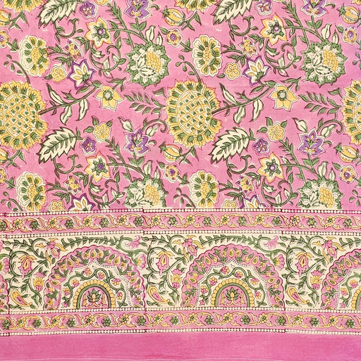Block-printed cotton tablecloth featuring yellow, green, and purple botanical motifs on a bubblegum pink background.