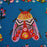 Colorful embroidered moth design on a blue fabric background with floral patterns.
