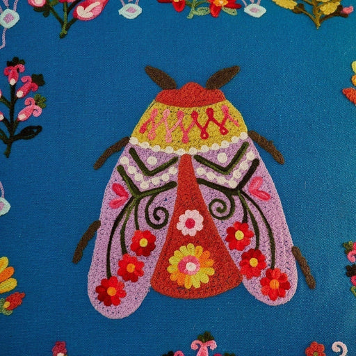 Colorful embroidered moth design on a blue fabric background with floral patterns.
