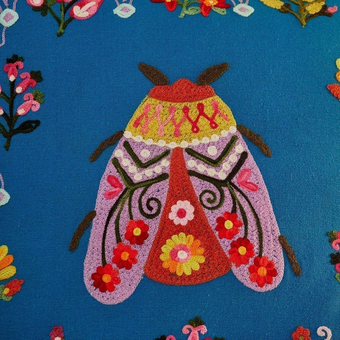Colorful embroidered moth design on a blue fabric background with floral patterns.