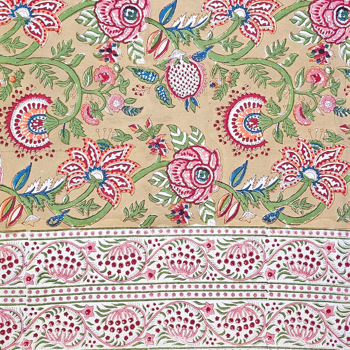 Top-down view of a Crimson Anar Sanganeri hand-block printed cotton tablecloth featuring a wide terracotta red floral border and a warm sand-colored background