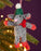Knitted mouse ornament with green hat and red scarf hanging on a Christmas tree.