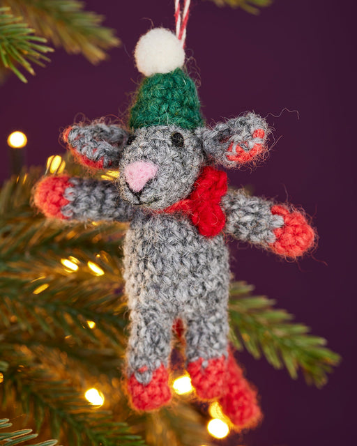 Knitted mouse ornament with green hat and red scarf hanging on a Christmas tree.