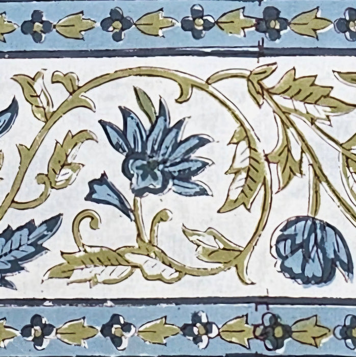 Close up detail of the border of a white cotton tablecloth hand-block printed with soft blue flowers and sage green leaves.