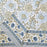 A folded white cotton tablecloth hand-block printed with soft blue flowers and sage green leaves.