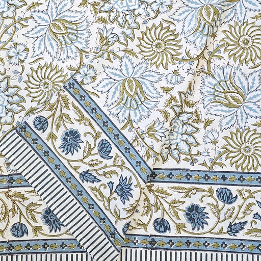 A folded white cotton tablecloth hand-block printed with soft blue flowers and sage green leaves.