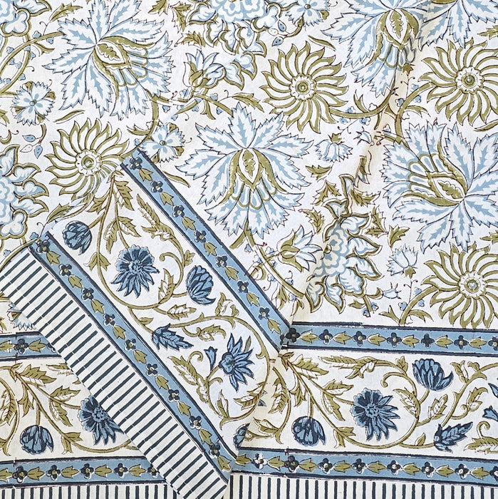 A folded white cotton tablecloth hand-block printed with soft blue flowers and sage green leaves.
