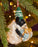 Knitted sheep decoration with a green hat hanging on a Christmas tree.