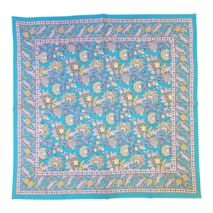 A square turquoise-blue tablecloth with an intricate multicolour floral pattern, featuring yellow, pink, and purple details, laid flat against a white background.