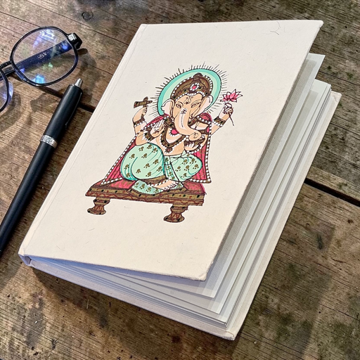 Notebook with a colourful illustration of Ganesh on a wooden surface with glasses and a pen.