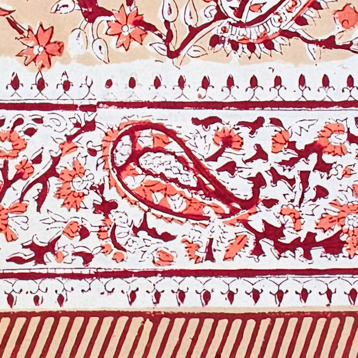 A close-up of a printed cotton tablecloth border featuring red and orange paisley and floral motifs on a warm peach background.