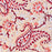 A close-up of a printed cotton tablecloth featuring red and orange paisley and floral motifs on a warm peach background.