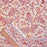 A folded section of a printed cotton tablecloth featuring red and orange paisley and floral motifs on a warm peach background, with a decorative border running horizontally across the lower portion.