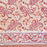 A close-up of a printed cotton tablecloth featuring red and orange paisley and floral motifs on a warm peach background, with a decorative border running horizontally across the lower portion.
