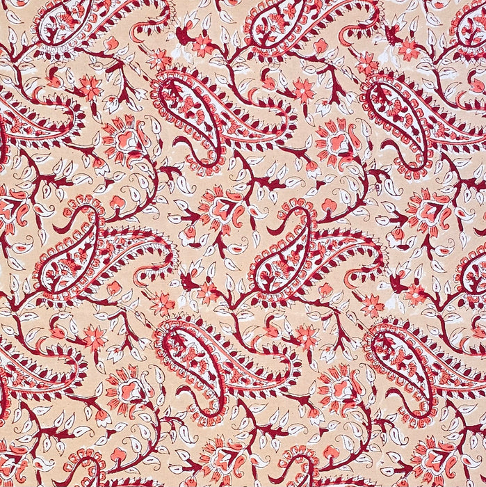 A close-up of a printed cotton tablecloth featuring red and orange paisley and floral motifs on a warm peach background.