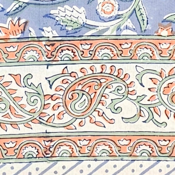 Close up picture of the border of a blue block printed cotton tablecloth with a green and orange floral design.