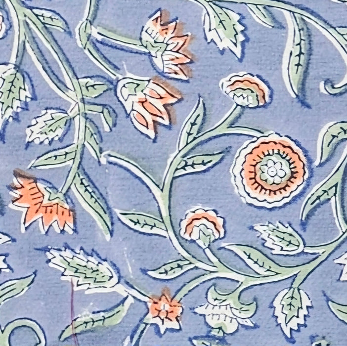 Deailed picture of a blue block printed cotton tablecloth with a green and orange floral design.