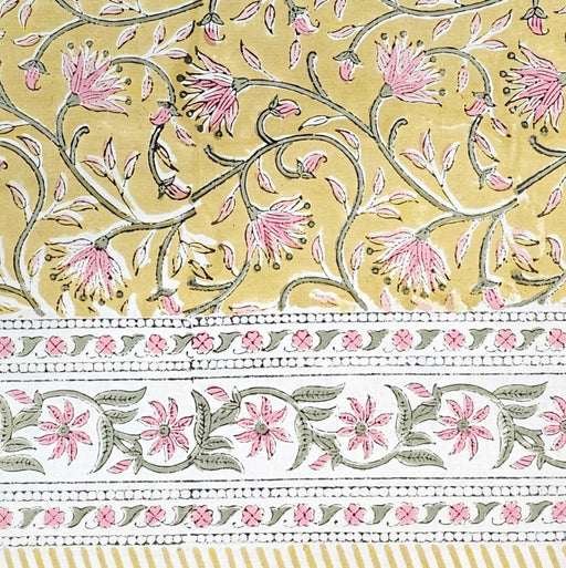 Block print tablecloth with yellow background and floral patterns in pink and green with a floral border.