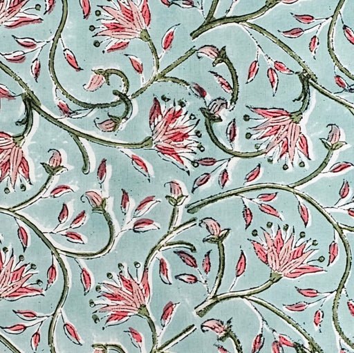 A square block-printed tablecloth featuring a floral pattern in shades of pink and green, on a pale turquoise background.