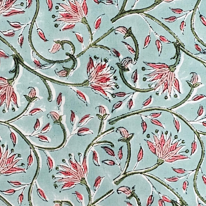 A square block-printed tablecloth featuring a floral pattern in shades of pink and green, on a pale turquoise background.