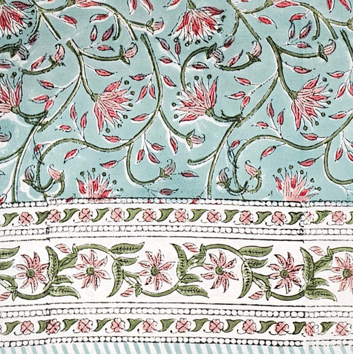 Block printed tablecloth with a pink and green floral design on a pale turquoise background and a white floral border