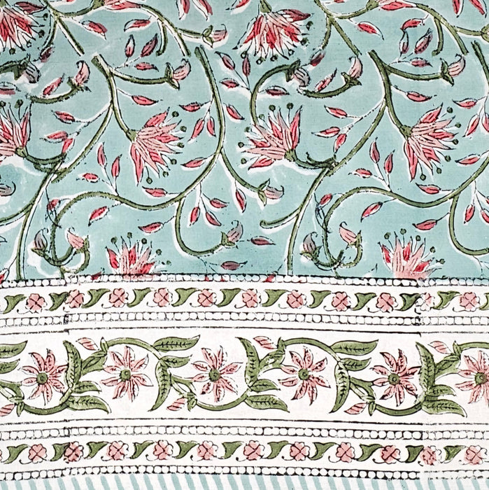 Block printed tablecloth with a pink and green floral design on a pale turquoise background and a white floral border