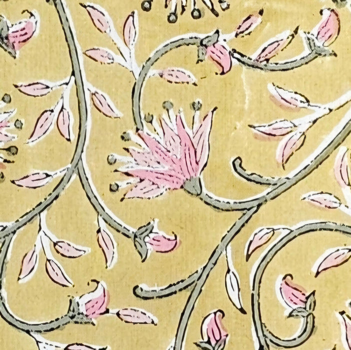 close up of a block print marigold design floral tablecloth in pink and green on a yellow background.