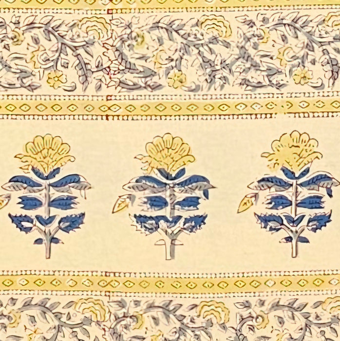 Detailed picture showing the border of a hand block printed tablecloth with a blue and grey foral design on a mustard yellow background.