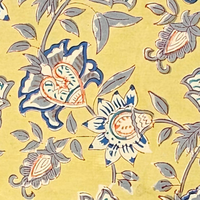 A close up picture of a hand block printed tablecloth with a blue and grey foral design on a mustard yellow background.