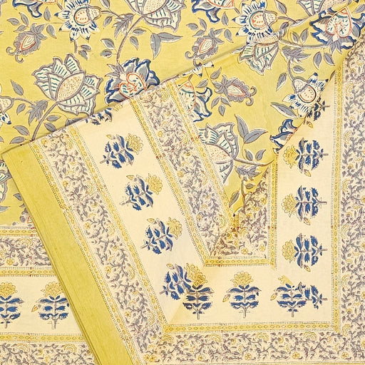 A hand block printed tablecloth with a blue and grey foral design on a mustard yellow background, folded back at one corner.