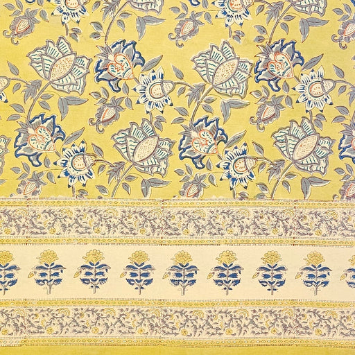 A hand block printed tablecloth with a blue and grey foral design on a mustard yellow background.
