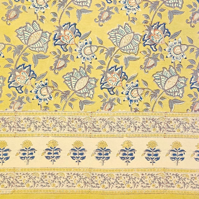 A hand block printed tablecloth with a blue and grey foral design on a mustard yellow background.