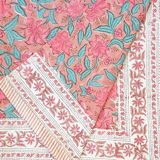 Hand block printed cotton tablecloth with a pink lily design and green leaves on an earthy pink background.  One corner of the tablecloth is folded back.