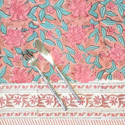 Hand block printed cotton tablecloth with a pink lily design and green leaves on an earthy pink background.  A knife and fork are shown to indicate the size of the pattern