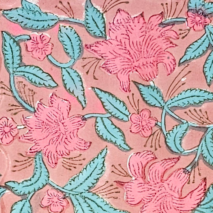 A close up picture of a block printed cotton tablecloth with a pink lily design and green leaves on an earthy pink background.  