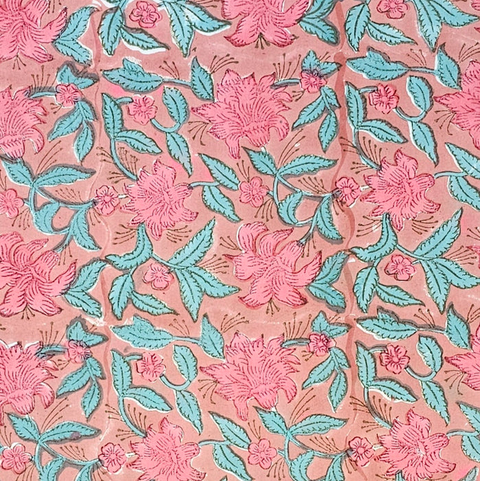 A block printed cotton tablecloth with a pink lily design and green leaves on an earthy pink background.