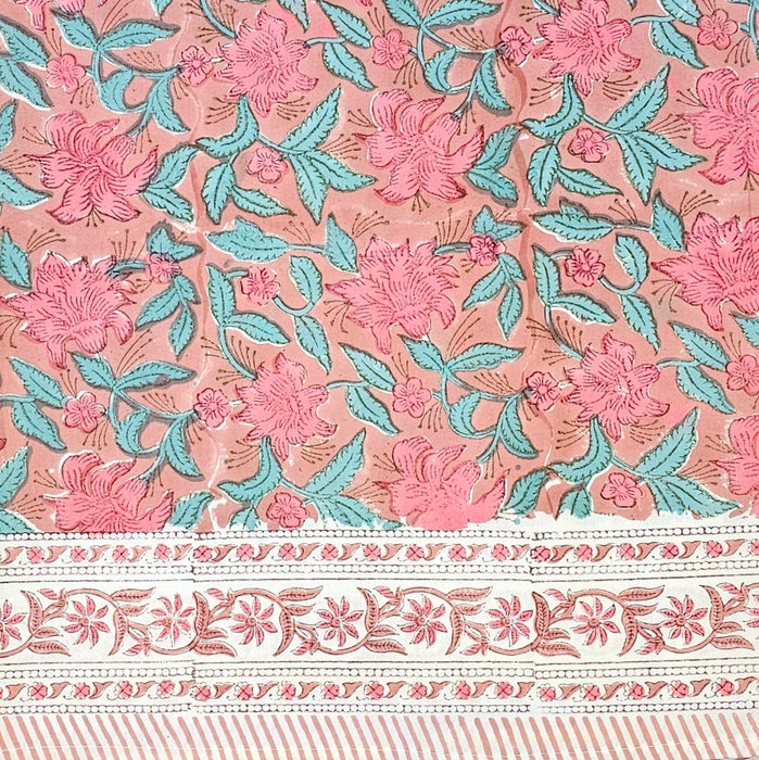Hand block printed cotton tablecloth with a pink lily design and green leaves on an earthy pink background.  The border of the tablecloth can be seen.