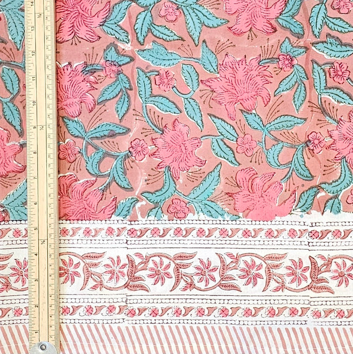 Hand block printed cotton tablecloth with a pink lily design and green leaves on an earthy pink background.  A meter ruler gives the scale of the pattern.