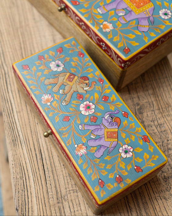 Two colourful wooden boxes with elephant illustrations on a wooden surface